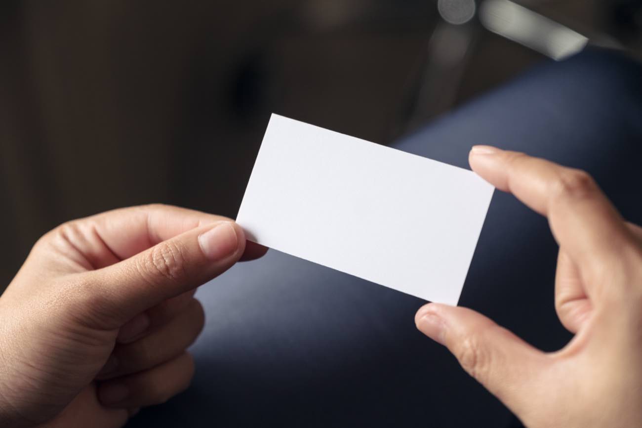 A business card being handed from one person to another, showing the card at real scale in the hand