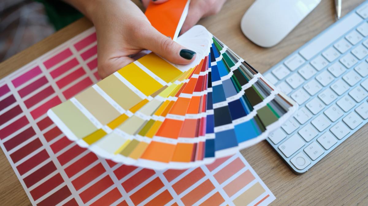 Designer's hands fanning out colorful printed sample swatches over a worktable